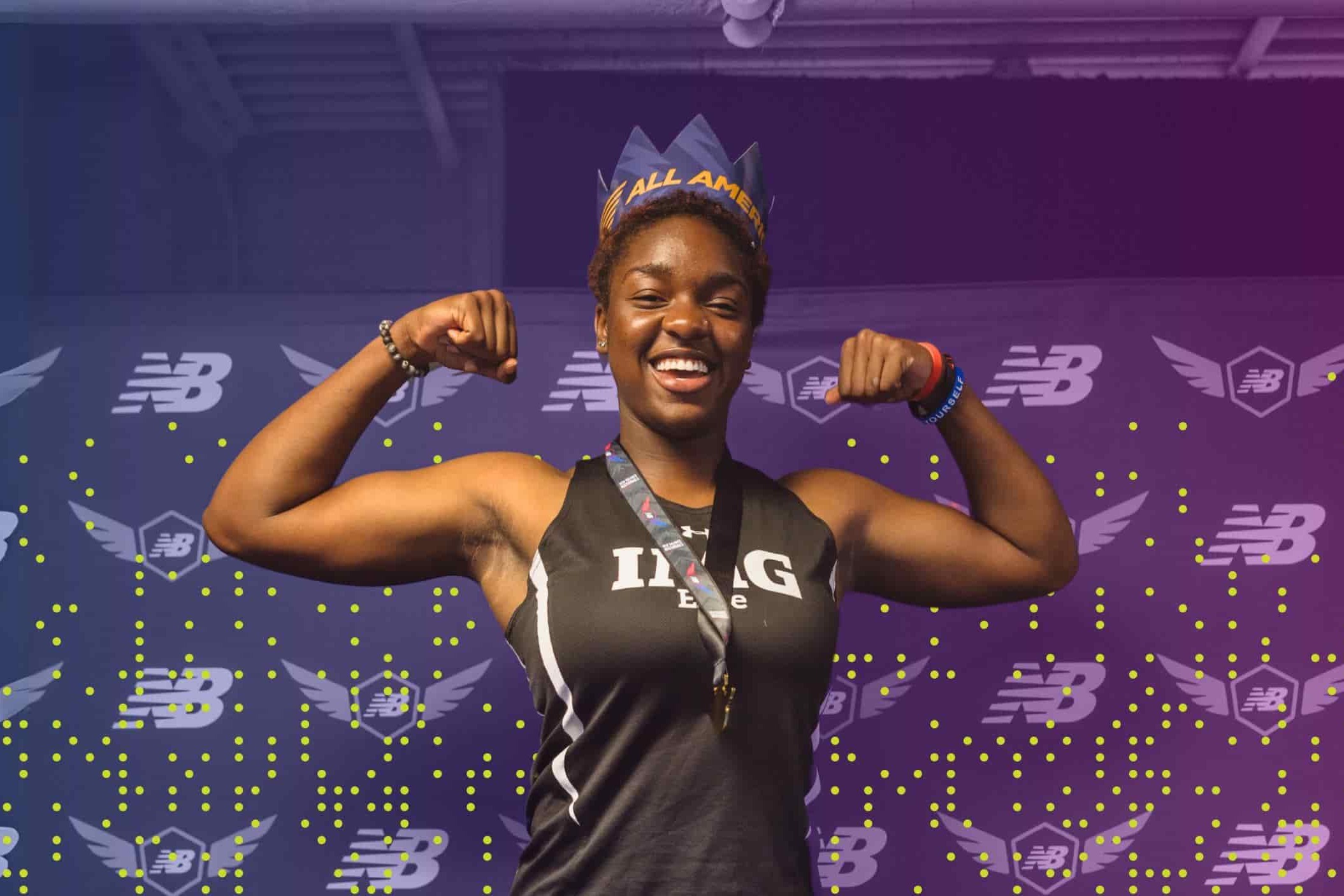 A confident student-athlete in an IMG uniform smiles and flexes her arms while wearing a crown labeled "All American." She stands in front of a branded New Balance backdrop, celebrating her athletic achievement.