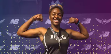 A confident student-athlete in an IMG uniform smiles and flexes her arms while wearing a crown labeled "All American." She stands in front of a branded New Balance backdrop, celebrating her athletic achievement.