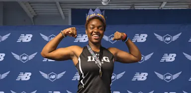 A smiling athlete flexes both arms in front of a sports-event backdrop.