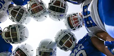 Helmeted football players lean together in a huddle viewed from below.