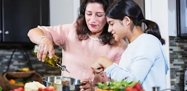 Mother and daughter cooking together in a modern kitchen, pouring olive oil and preparing a healthy meal vegetarian meal.