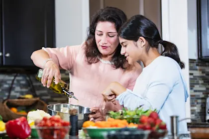 Mother and daughter cooking together in a modern kitchen, pouring olive oil and preparing a healthy meal vegetarian meal.