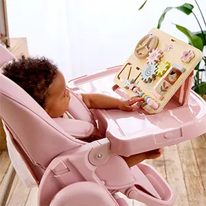 Toddler sitting in the pink Puggle Feed & Play highchair, playing with the wooden toy stand on the tray.