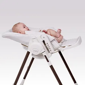 Baby lying in the Puggle Feed & Play highchair with the seat fully reclined into a cradle position.