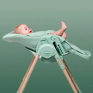 Baby lying in the pistachio green Puggle Feed & Play highchair with the seat fully reclined into a cradle position.