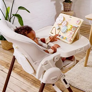 Toddler sitting in the Puggle Feed & Play highchair, reaching towards the wooden toy stand on the tray.