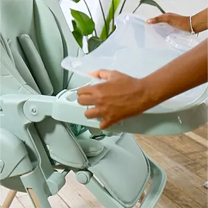 Two hands lifting the removable tray insert off the pistachio green Puggle Feed & Play highchair.