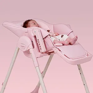 Baby lying in the pink Puggle Feed & Play highchair with the seat fully reclined into a cradle position.