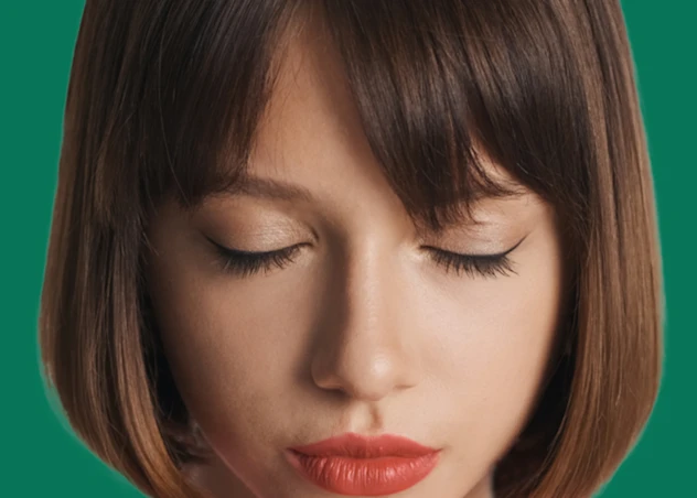A woman with fair skin and a brown blunt cut bob hairstyle is closing her eyes.