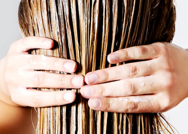 Woman with fair skin holds her shimmering light brown hair.
