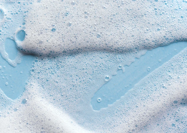 Lush white lather on a vibrant blue background, symbolizing effective cleansing and ideal shampoo products for low porosity hair.