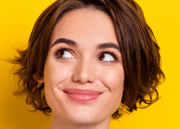 A woman with fair skin, a square face and short brown hair grins while looking up in front of a yellow background.
