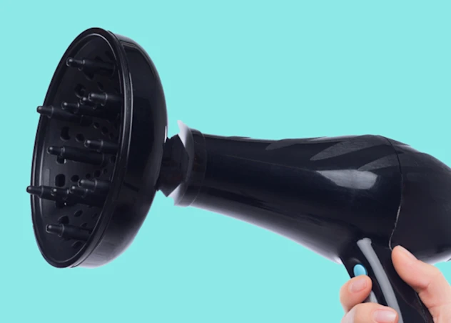 A blow dryer diffuser is being held up and faced to the left in from of a turquoise background.