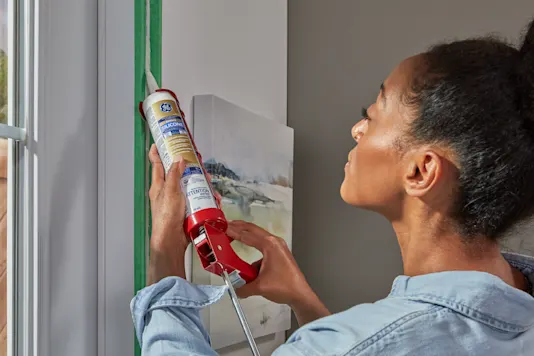 Image d’une femme appliquant du calfeutrage autour des moulures d’une fenêtre.