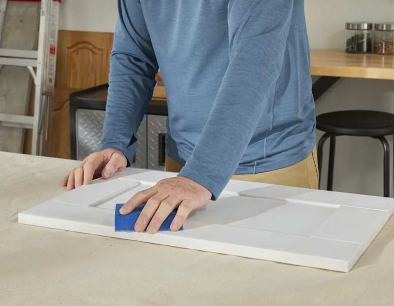 A man scuff-sands the primed cabinets