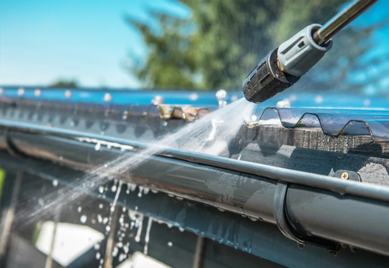 A homeowner cleaning gutters with a pressure washer
