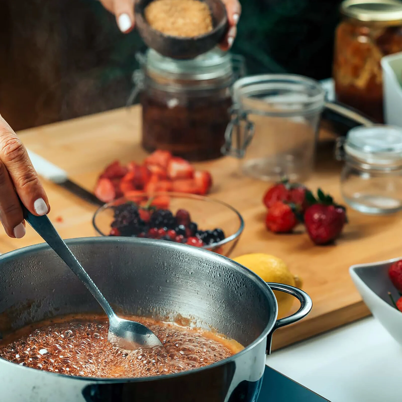 Person making jam in a pot in the kitchen.