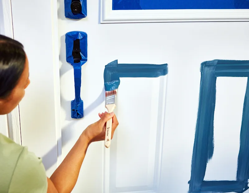 A person painting a front door with a paint brush.