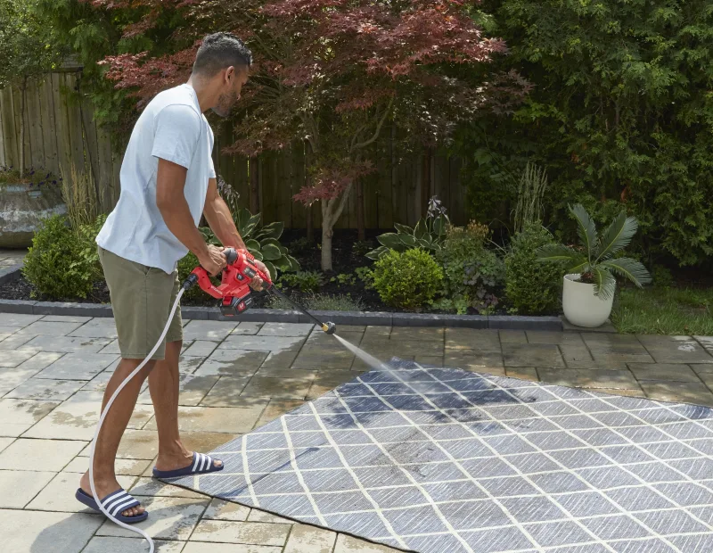 A man washes rug with a power washer