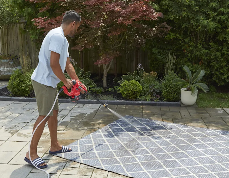 Un homme lave un tapis avec une laveuse a pression