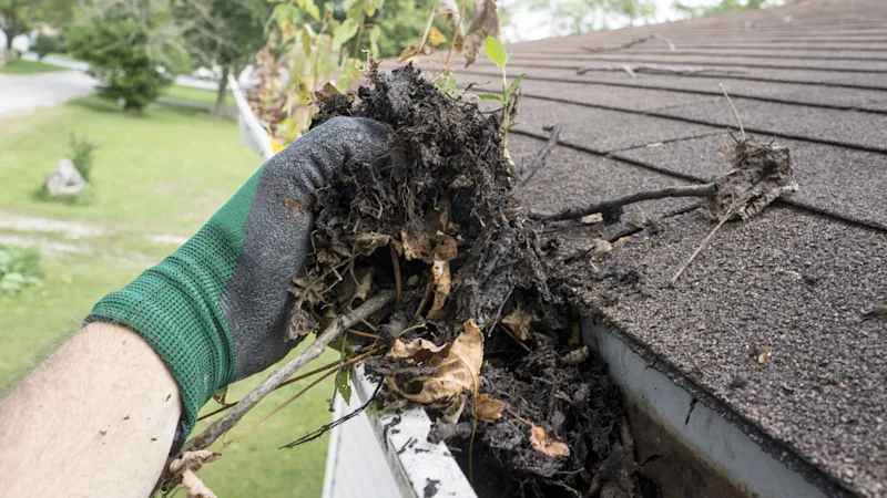 travailleur enlevant les feuilles de la gouttière