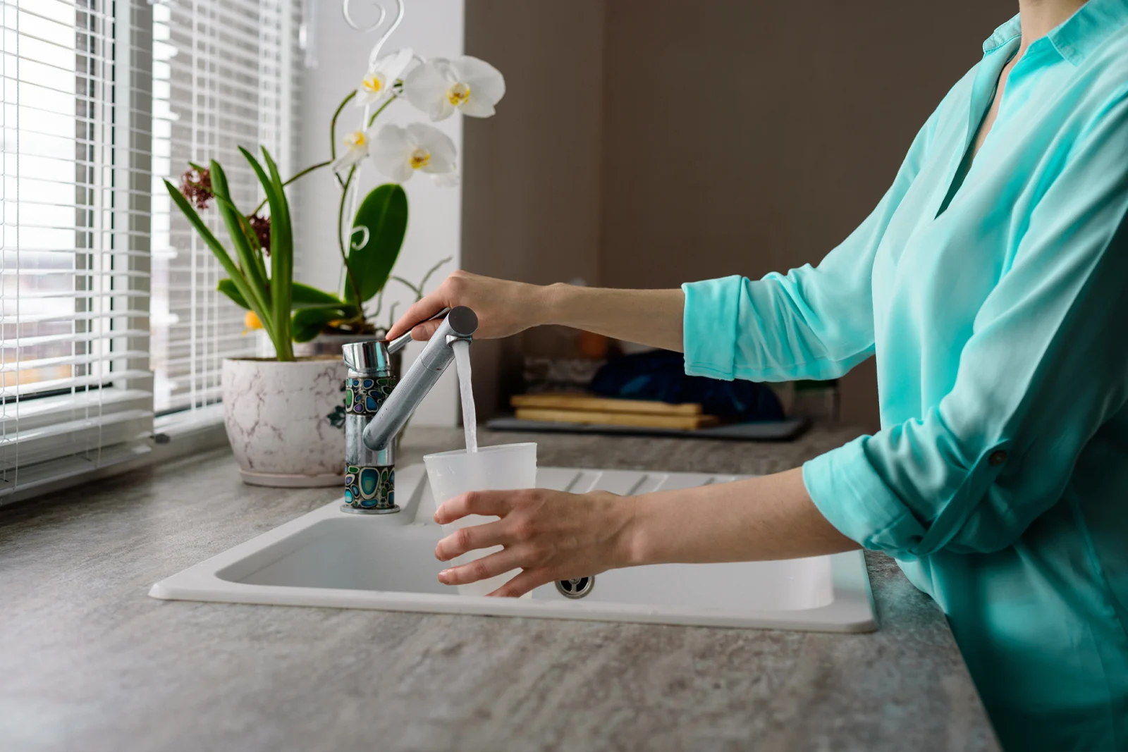 Une femme prenant un verre d’eau au robinet de la cuisine.