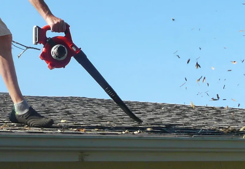 A homeowner cleaning gutters with a leaf blower
