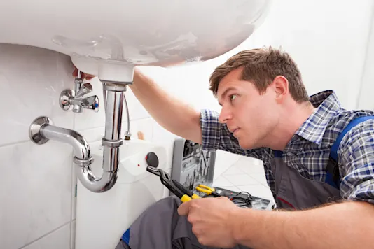 Un plombier inspectant l’installation de plomberie d’un évier de salle de bain.