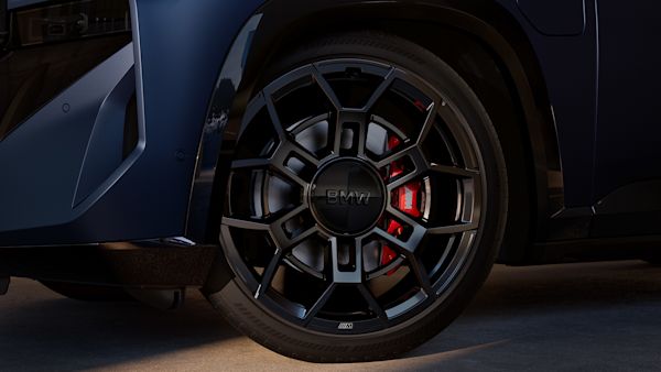Close-up of a BMW car's front wheel and tire, showcasing the intricate black alloy rim design with visible red brake calipers.