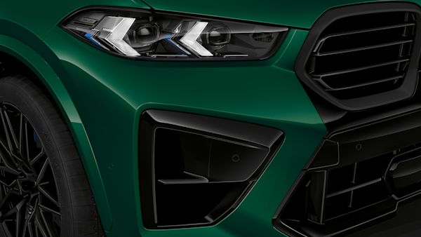 Close-up of the front right side of a green BMW SUV, showing the headlight, grille, and part of the front wheel.