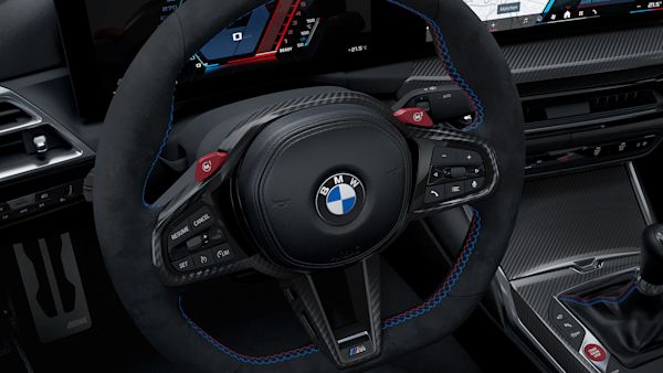 Close-up view of a BMW car's interior, focusing on the steering wheel with the BMW logo, dashboard displays showing navigation maps and vehicle information, and part of the gear shift.