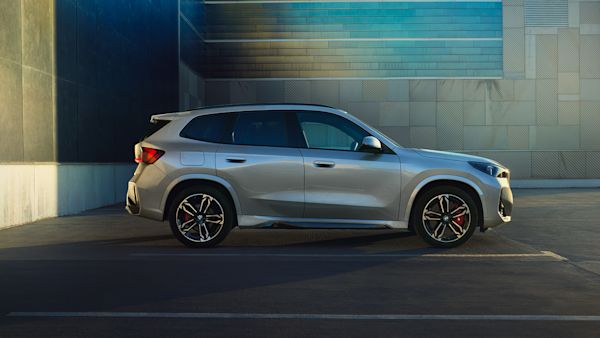 A white BMW SUV parked in an empty parking lot next to a modern building with a blue and beige facade during sunset.