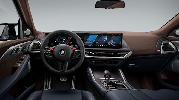 Interior view of a modern BMW car showing the steering wheel, dashboard with digital displays, gear shift, and luxurious leather seats.