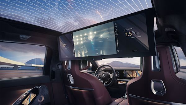 Interior of a luxury BMW car with a panoramic sunroof, featuring a large digital screen mounted behind the front seats displaying 1.5°C temperature and an image of a person playing the piano.