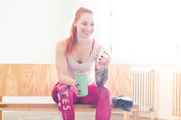 Girl with red hair and tattoos in workout gear, holding smartphone