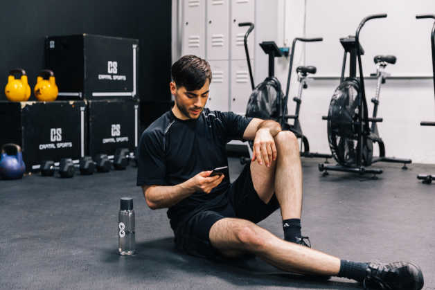 Man sitting with phone at the gym, next to 8fit bottle