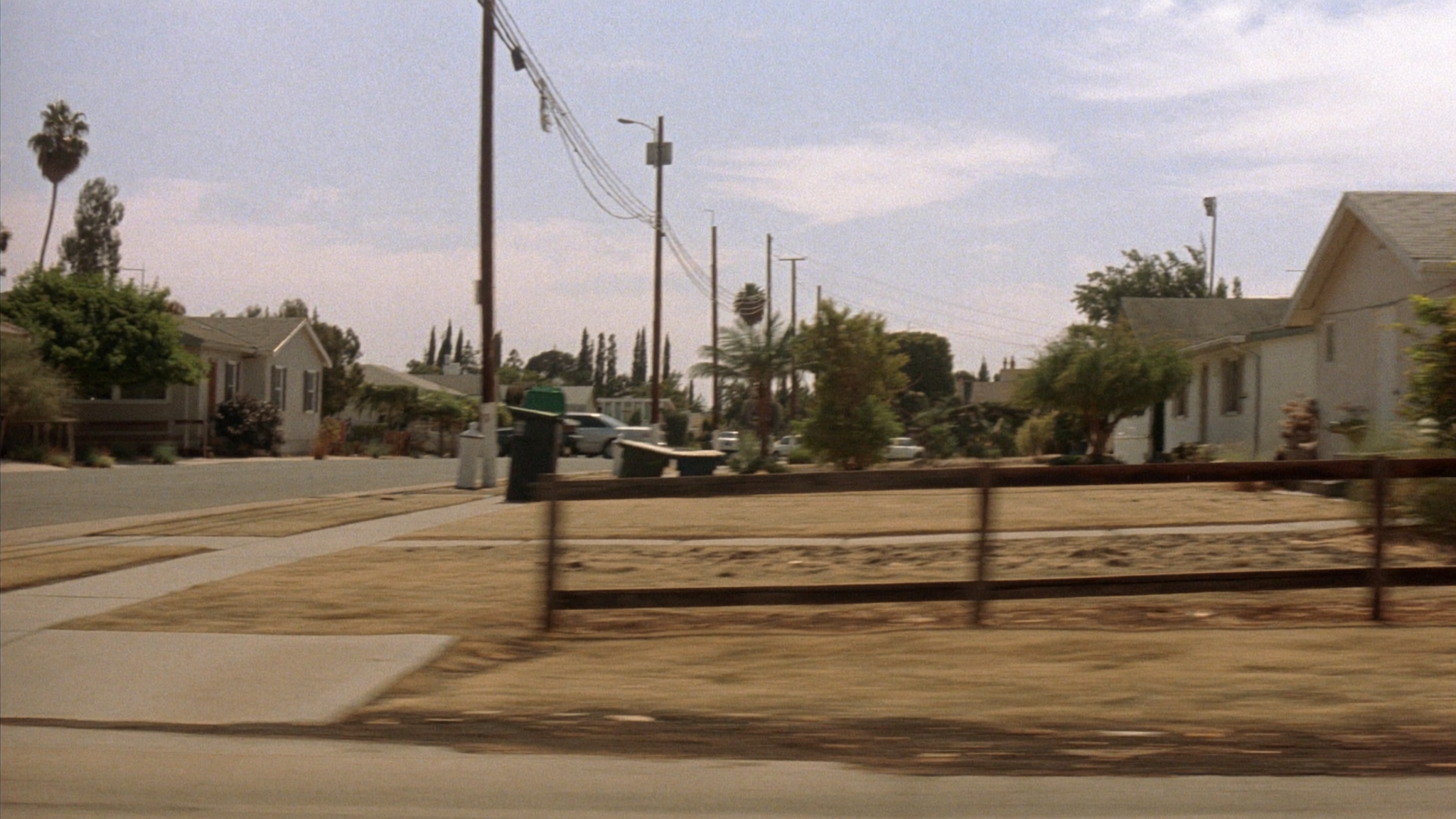 Quiet suburban street in an LA-style neighborhood, viewed from the side window of a moving car