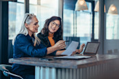 Two women analyzing documents while sitting on a table in office