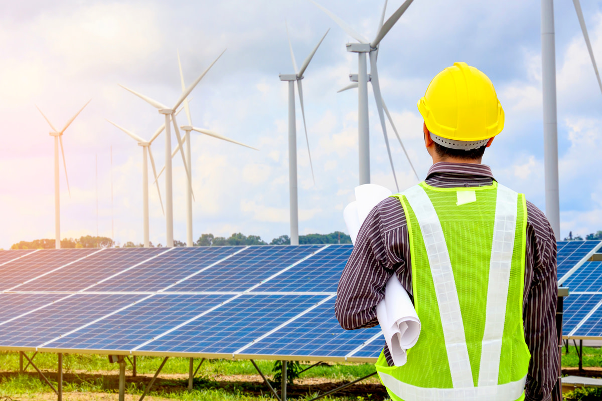 Young business man engineer with yellow helmet at solar panel and wind generators power plant construction