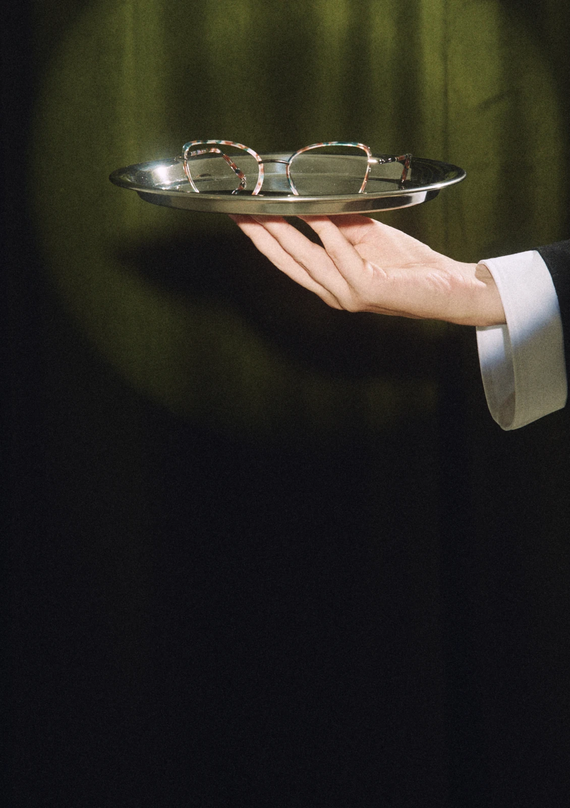 Hand holding out glasses on a silver tray, AW26 collection
