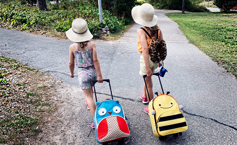 Två barn har resväskor med sig på sommaren.