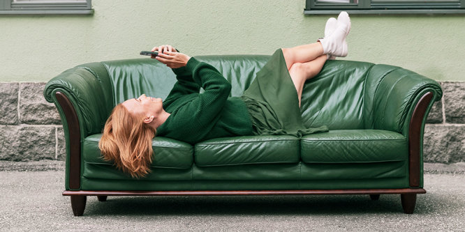 En kvinna vilar på soffan med en telefon i handen.