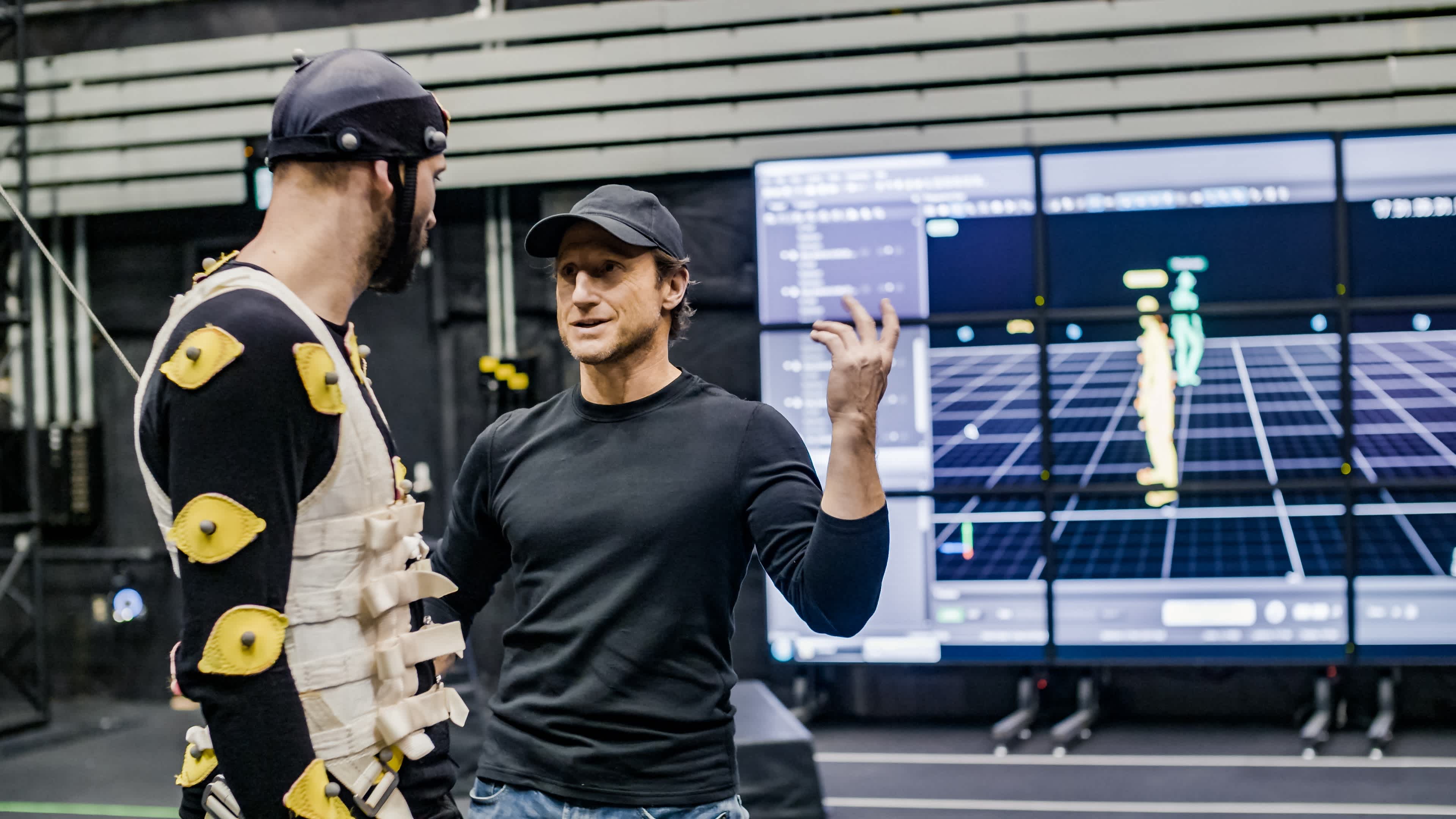 Director on motion capture set giving explaining something to an actor. 
