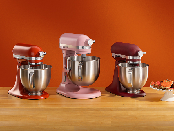 A red stand mixer, a pink stand mixer and a deep red stand mixer on a wooden counter