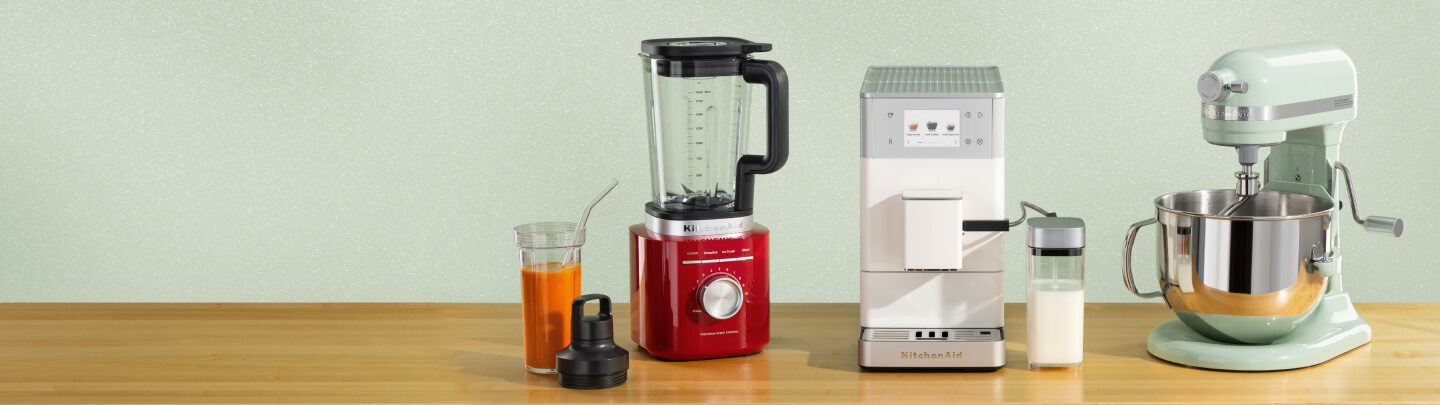 A red blender, white espresso machine and aqua stand mixer on a wooden counter with a smoothie in the blender jar.