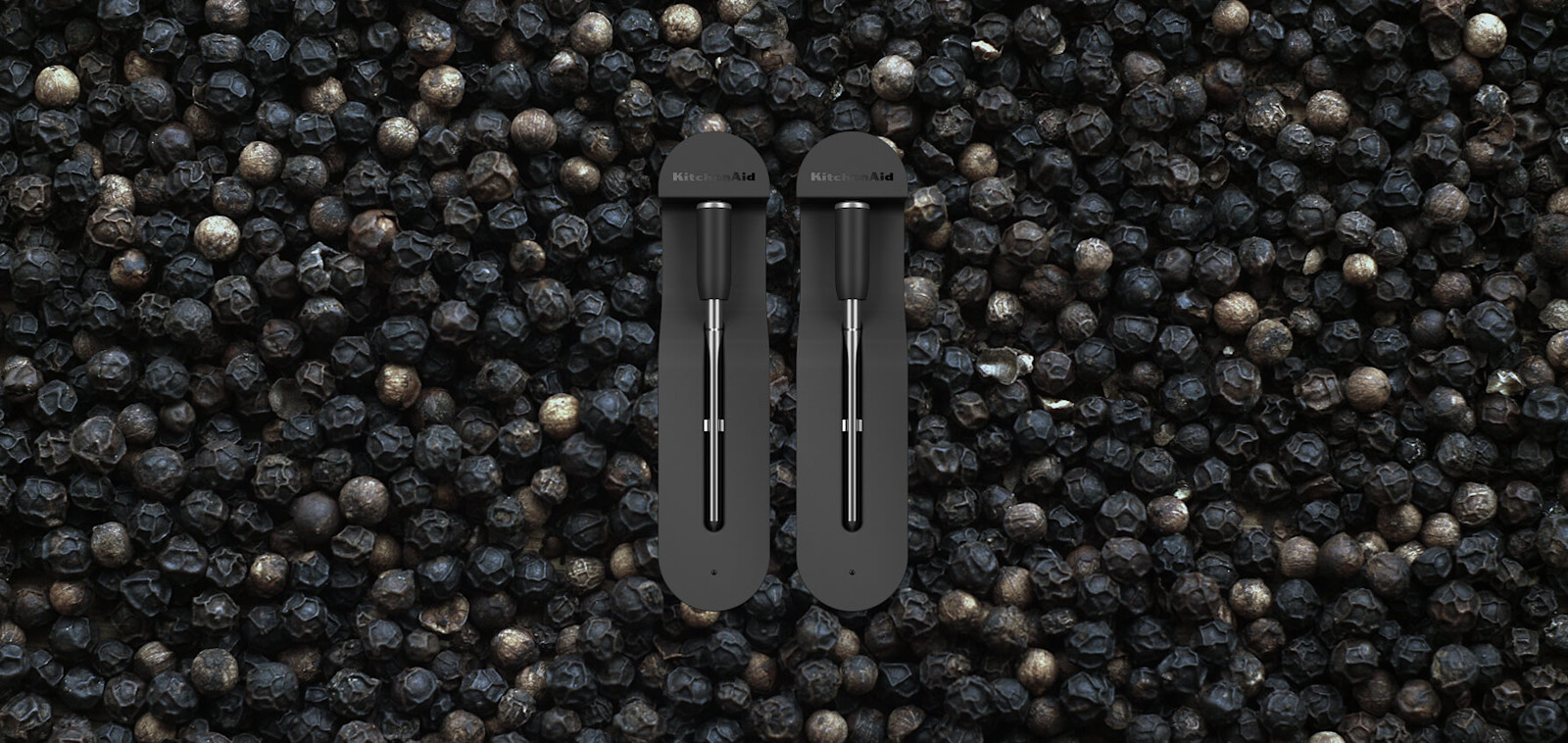 A KitchenAid® Smart Thermometer against a background of peppercorns