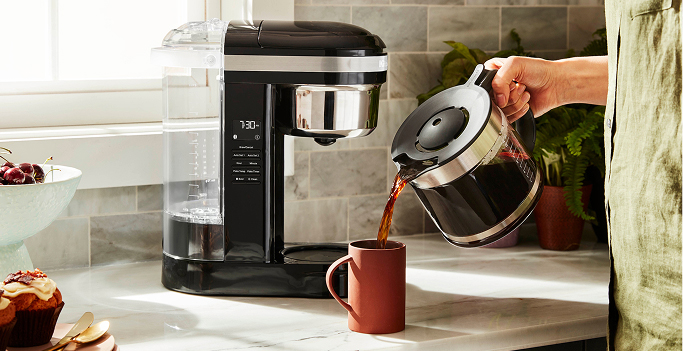 A person pouring coffee from a drip coffee maker into a mug.