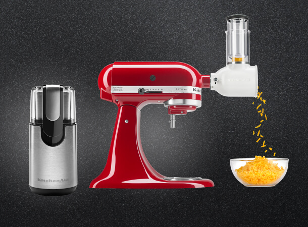 Black KitchenAid® coffee grinder beside a red KitchenAid® stand mixer with a slicer/shredder attachment producing shredded cheese