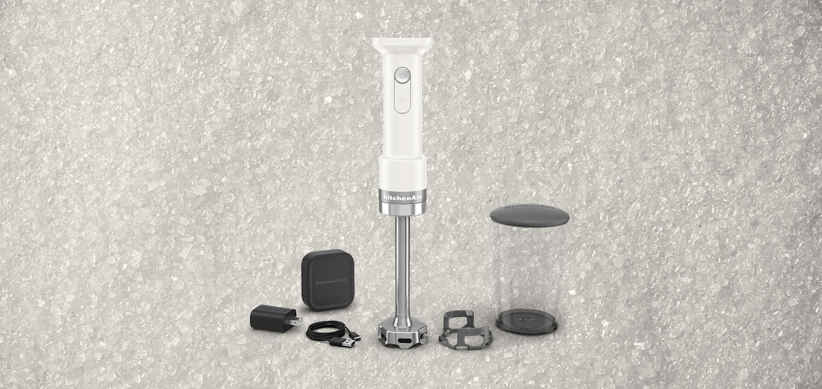 White KitchenAid® hand blender with attachments, against a background of coarse salt