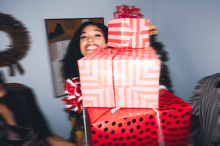 Woman smiling and holding wrapped holiday gifts in front of a Christmas tree